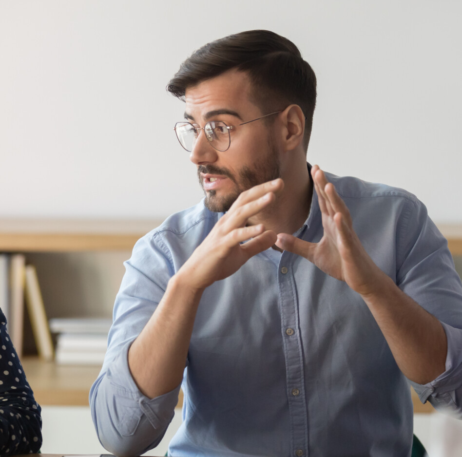 Confident male boss explaining ideas to diverse team at office Confident male leader or mentor in eyeglasses looking at young indian female employee, explaining project ideas, communicating with teammates, discussing work issues or providing workshop at office.